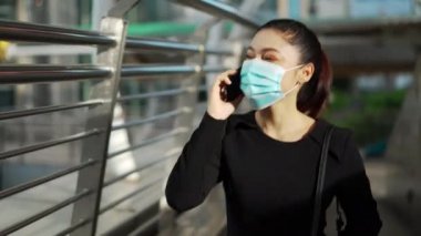 İş kadını akıllı telefonla konuşuyor ve Coronavirus (covid-19) salgınından korunmak için tıbbi maske takıyor.