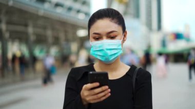 Şehirdeki Coronavirus (covid-19) salgınından korunmak için akıllı telefon kullanan ve tıbbi maske takan bir iş kadını
