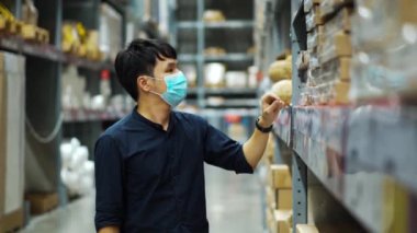 Tıbbi maskeli bir işçi Coronavirus (covid-19) salgını sırasında depoda envanter kontrolü yapıyor..