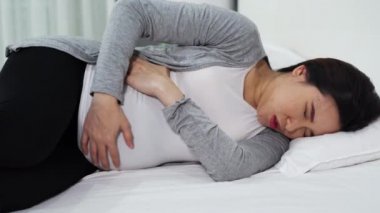 Hamile bir kadının yatakta karnı ağrıyor.