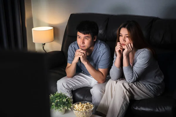 crying young couple watching romantic movie TV on sofa at night