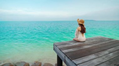 Koh MunNork Adası, Rayong, Tayland 'da kolları havada, tahta bir köprüde oturan mutlu kadın. 
