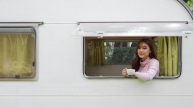 Karavan karavanının vitrininde kahve içen mutlu genç bir kadın.