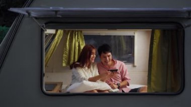 Genç bir çift, gece karavan karavanının yatağında akıllı telefon kullanıyor.