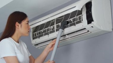 Evdeki klimayı temizlemek için elektrik süpürgesi kullanan genç bir kadın.