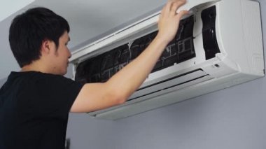 Genç adam evdeki temizlik için klimanın hava filtresini kaldırıyor.