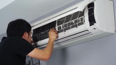 Genç adam temiz filtreyi klimaya yerleştiriyor.