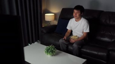 Genç adam geceleri kanepede televizyon izliyor.