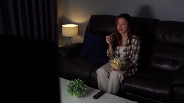 Забавная Молодая Женщина Смотрит Телевизор Ест Попкорн Диване Ночью — стоковое видео