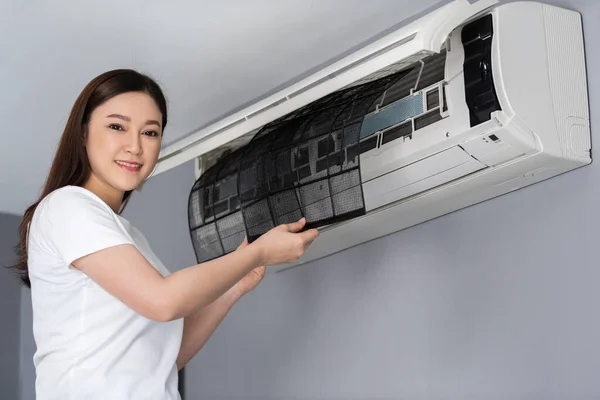 年轻女子在家中清除冷气机的空气过滤器 — 图库照片