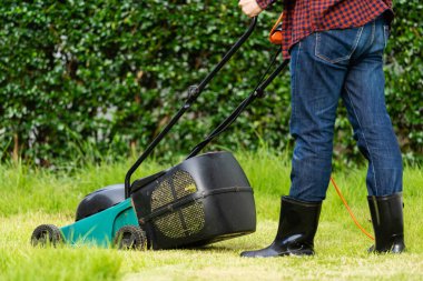 Evde çim biçme makinesi kullanan bir işçi.