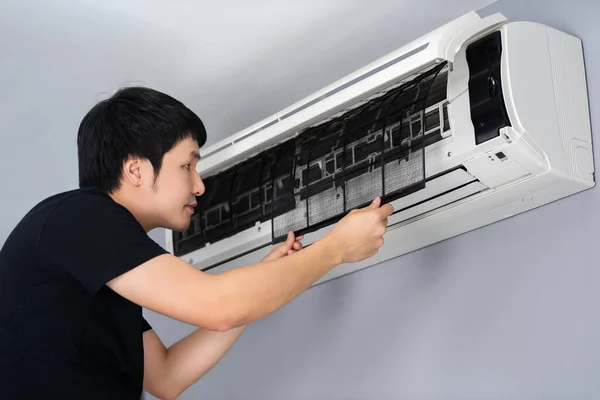 young man removing air filter of the air conditioner for cleaning at home