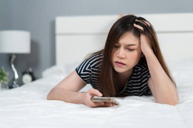 Stresli kadın yatakta akıllı telefon kullanıyor.