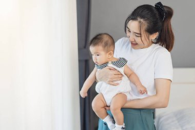 Anne yeni doğmuş bebeği kucağında tutuyor yatak odasının penceresinin yanında.
