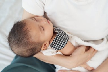 Anne kucağında yeni doğmuş bir bebek, kollarında bir yatakta uyuyor.