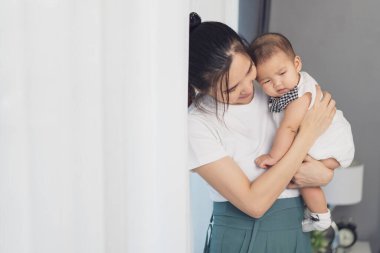 Anne yeni doğmuş bebeği kucağında tutuyor yatak odasının penceresinin yanında.