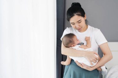 Anne kucağında bebek, yatak odasının penceresinin yanında kolunda uyuyor.