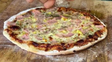 Elleri ağır çekimde kömürlü pizzaya kekik serpiyorlar.