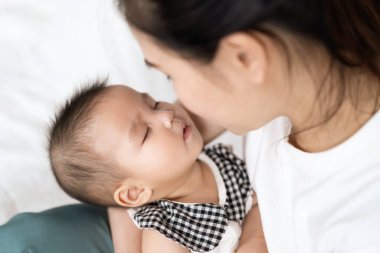 Anne kucağında yeni doğmuş bir bebek, kollarında bir yatakta uyuyor.