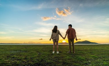 young couple holding hands in green field at sunset