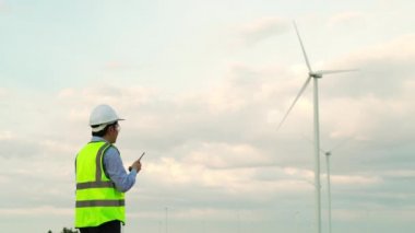Genç erkek mühendis telsiz kullanarak rüzgar türbini çiftliğini kontrol ediyor.