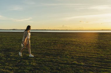 Neşeli kadın yeşil arazide gün batımıyla yürüyor.