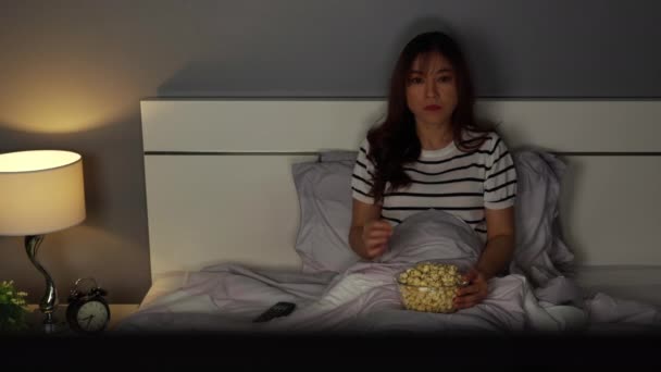 schockierte junge Frau schaut nachts Horrorfilm-TV auf einem Bett