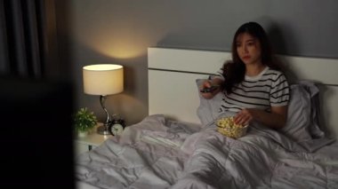 Genç bir kadın TV seyrediyor ve geceleri yatakta patlamış mısır yiyor.