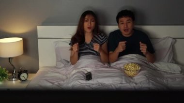 Üzgün genç bir çift spor televizyon seyrediyor ve geceleri yatakta maç kaybediyor.