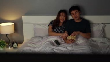 Genç bir çift TV seyrediyor ve geceleri yatakta patlamış mısır yiyor.