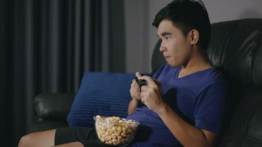 Genç adam geceleri oturma odasında joystick ile video oyunu oynuyor.