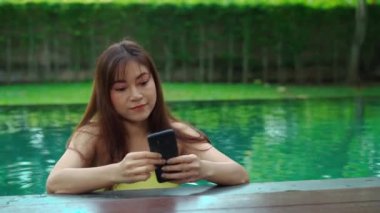 Mutlu kadın yüzme havuzunda fotoğraf çekmek için akıllı telefon kullanıyor.