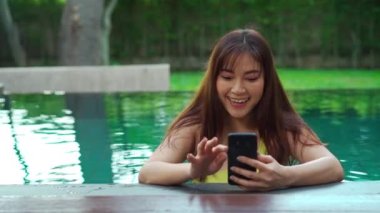 Havuzda akıllı telefon kullanan mutlu bir kadın.
