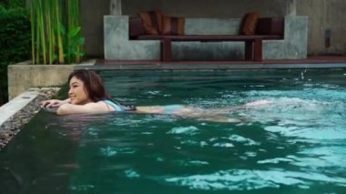 Kadının ağır çekimde yüzme havuzunun kenarına tutunması ve ayaklarıyla su sıçratması.