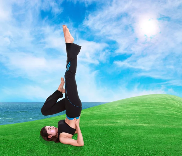 Frau macht Yoga-Übungen auf Gras mit Himmel — Stockfoto
