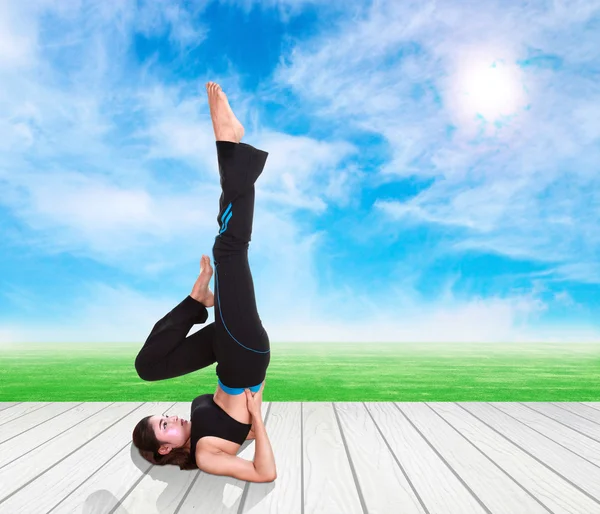 Woman doing yoga exercise on wood floor with green grass and sky — Stock Photo, Image