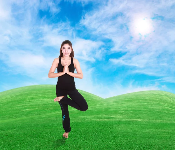 Frau macht Yoga-Übungen auf Gras mit Himmel — Stockfoto