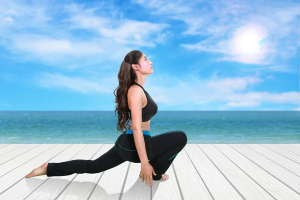 Mujer haciendo ejercicio de yoga sobre suelo de madera con mar y cielo — Foto de Stock