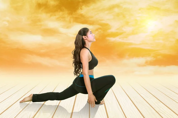 Mulher fazendo exercício de ioga no chão de madeira ao pôr do sol — Fotografia de Stock