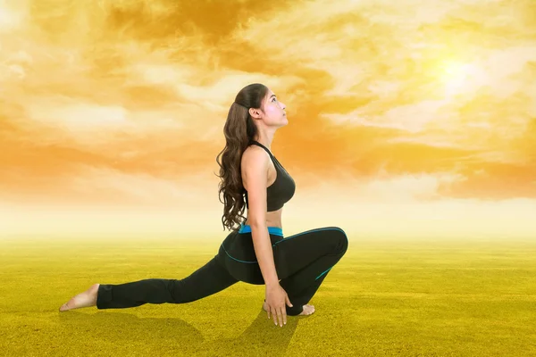 Frau macht Yoga-Übungen im Gras bei Sonnenuntergang — Stockfoto