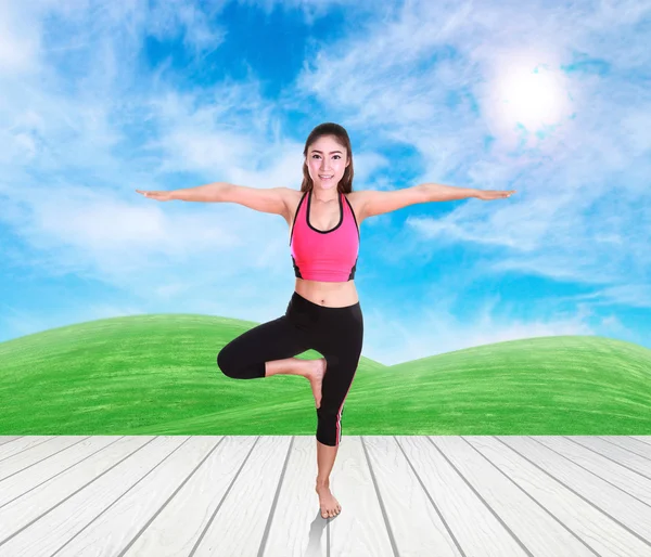 Kobieta robi ćwiczenia jogi na podłogi z drewna z zieloną trawą i niebo — Zdjęcie stockowe