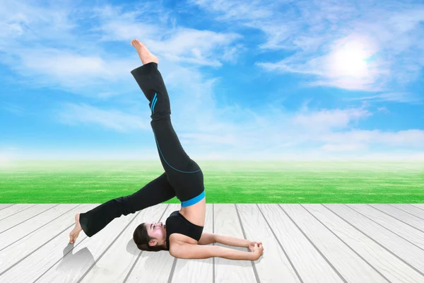 Mujer haciendo ejercicio de yoga sobre suelo de madera con hierba verde y cielo — Foto de Stock