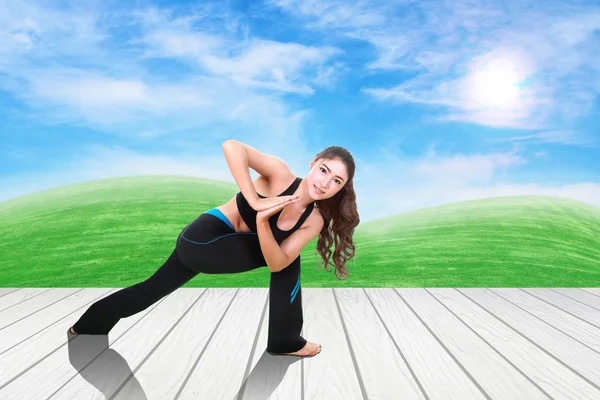 Mujer haciendo ejercicio de yoga sobre suelo de madera con hierba verde y cielo — Foto de Stock