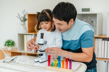 father and toddler girl scientist placing microscope slides with specimen. learning science at home