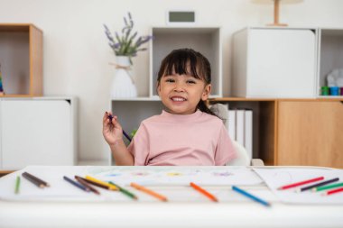 Yeni yürümeye başlayan bebek evde masa üstünde renkli kalemle çizim yapmayı öğreniyor.