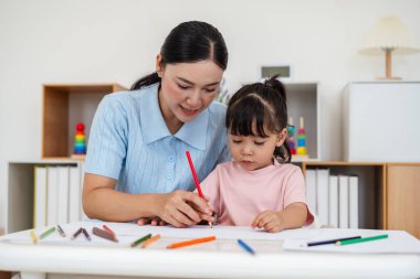 toddler baby girl training to drawing with colored pencil with mother helping on a desk at home