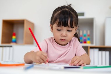 toddler baby girl training to drawing with colored pencil on a desk at home