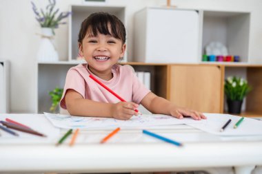 Yeni yürümeye başlayan bebek evde masa üstünde renkli kalemle çizim yapmayı öğreniyor.