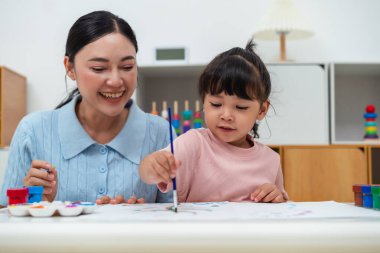 happy mother and toddler girl painting watercolor in a paper at home