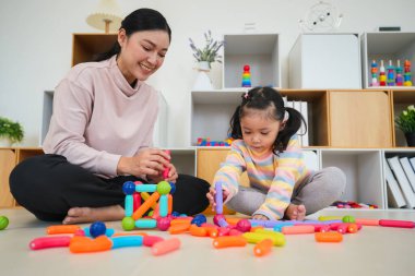Mutlu bebek kız ve anne evde renkli manyetik inşaat oyuncağı oynuyorlar.